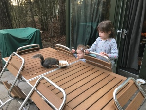 Outside on the patio table my nieces are sharing breakfast with a friendly squirrel. It is very close to them. 