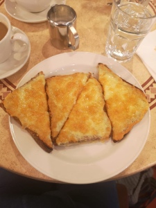 This photo is taken looking down on to a plate of cheese on toast. There are two slices of toast, each cut in half. Arranged attractively in triangles. 