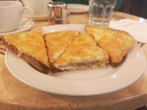 The same plate of cheese on toast. Photo taken from a side angle. Cheese is melting over the edges of the toast. 