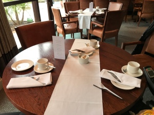 A photo taken looking down onto the large round table. There are plates at napkins at the place settings and a large window in the background. 