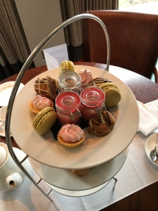 Looking down on to the top tier of desserts. There are three tarts, three macarons, three halves of choux bun and three small jars filled with pink posset. 