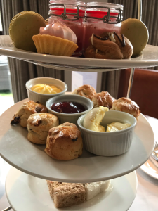 A close up of the afternoon tea stand, focussing on the scones. There a six mini scones with pots of cream, jam and butter. 